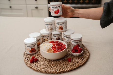 Yogurt bowl with raspberries, strawberries, coconut and white chocolate surrounded by Body&Fit Flavour Powder jars