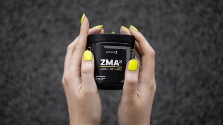 Hände mit schwarzer ZMA-Dose und gelbem Nagellack.