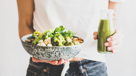 Person holding bowl of healthy salad and green smoothie bottle.