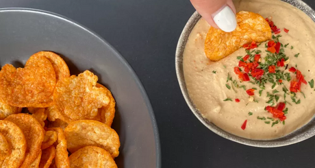 Hand dipping protein chip into spicy hummus.