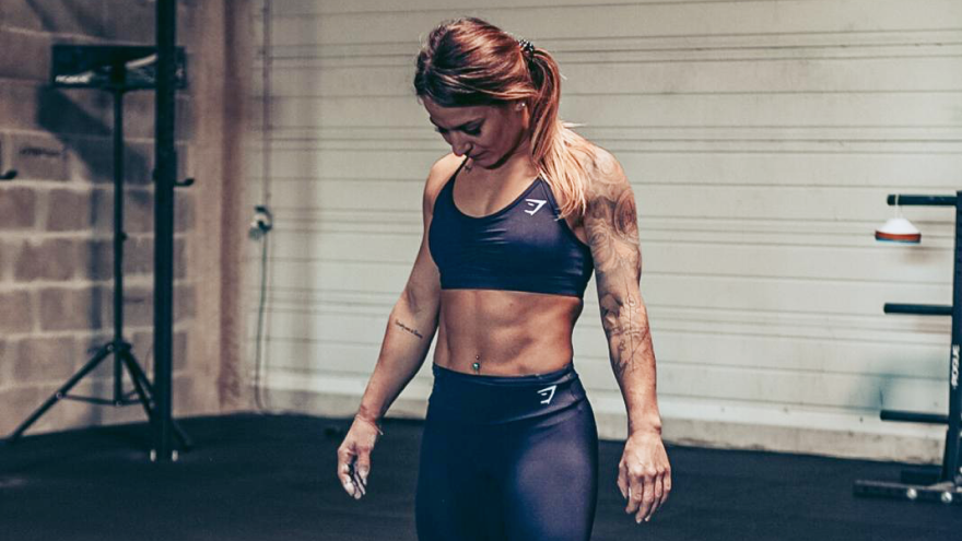 Vrouw in sportoutfit in gym kijkt omlaag.