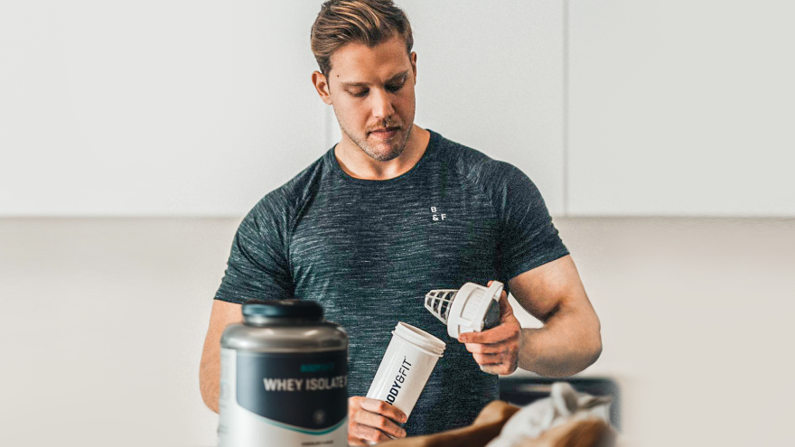 Man vult Body&Fit shaker met proteïnepoeder in keuken.