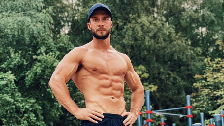 Uomo muscoloso a petto nudo posa all’aperto.