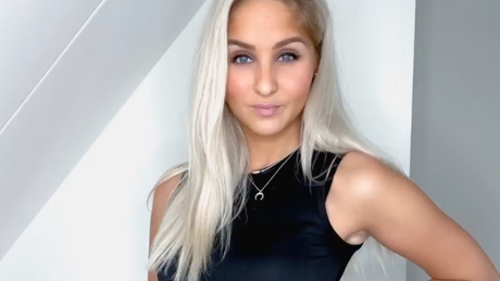 Fitness-Influencerin posiert in schwarzem Sportoutfit vor heller Wand.