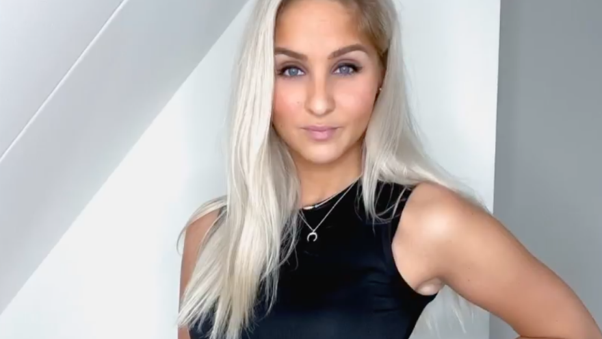 Vrouw poseert in zwarte sporttop met lang blond haar.