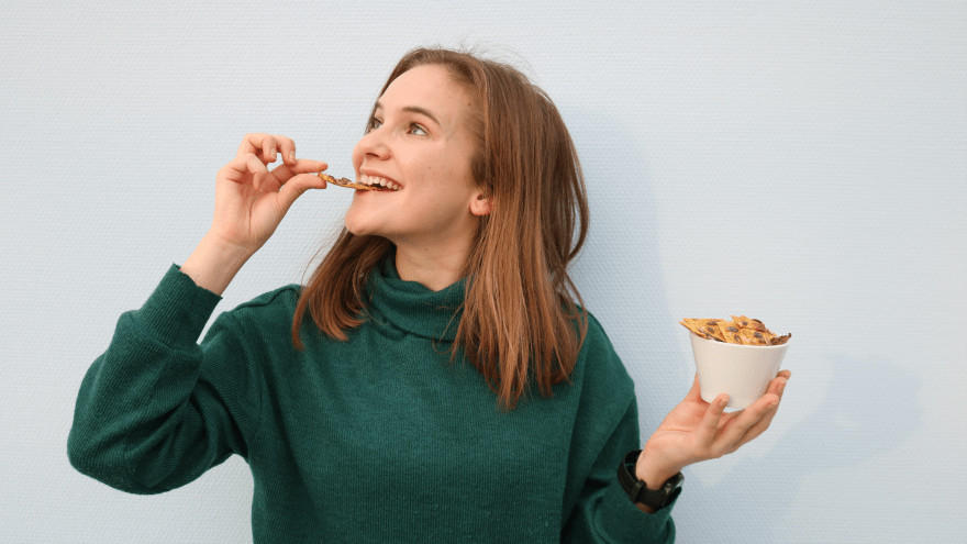 Vrouw eet gezonde snack uit bakje en lacht.