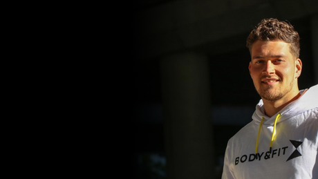 Man smiling in white Body&Fit hoodie under sunlight.