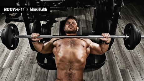 Man performing bench press with barbell in gym.