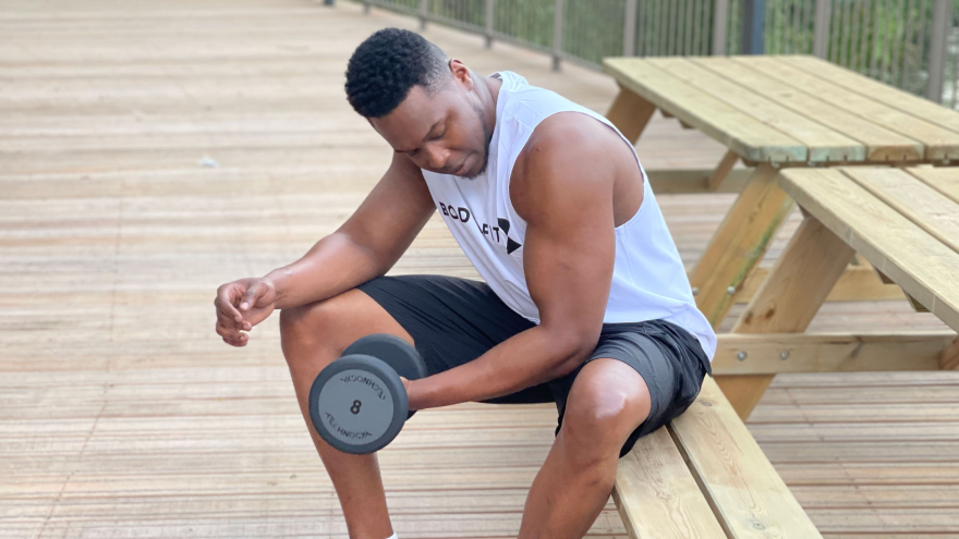 Homme en débardeur Body&Fit faisant des curls haltère.