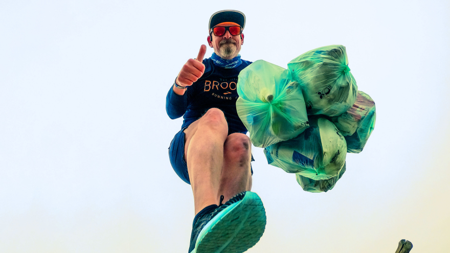 Mann hebt Daumen mit vollen Müllsäcken beim Plogging.