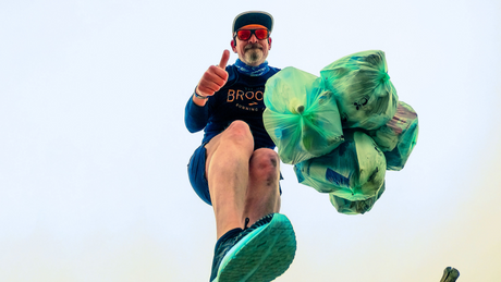 Mann hebt Daumen mit vollen Müllsäcken beim Plogging.