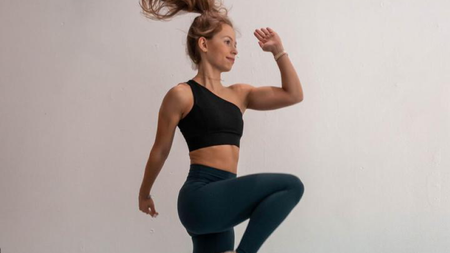 Femme en tenue de sport sautant devant un mur blanc.