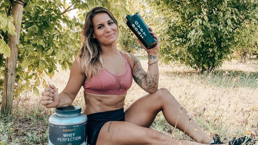 Sportlerin im Freien mit Proteinshake und Pulverdose.