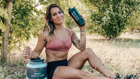 Sportlerin im Freien mit Proteinshake und Pulverdose.