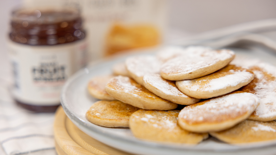 Poffertjes met poedersuiker op bord met fruitspread op achtergrond.