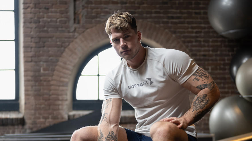 Muskulöser Mann in weißem Shirt sitzt nach Workout im Gym.