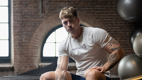 Muskulöser Mann in weißem Shirt sitzt nach Workout im Gym.