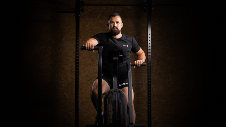 Mann trainiert auf Air Bike im Fitnessstudio mit dunklem Hintergrund.