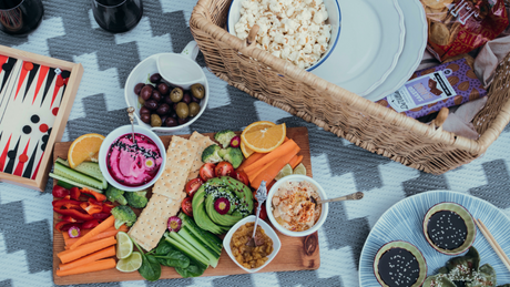 Colorful vegan picnic platter with dips, crackers, and fresh vegetables.