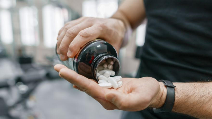 Hand schüttet weiße Kapseln aus Dose im Gym.