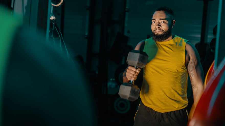 Man lifting dumbbell in gym wearing yellow tank top.