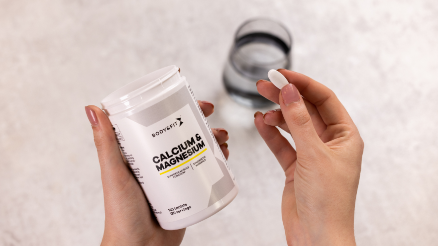 Hand mit Kalzium-Kapsel und Vitaminpräparatdose.