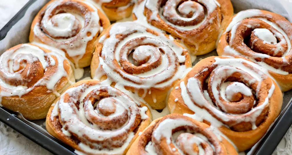 Versgebakken kaneelbroodjes met glazuur in ovenschaal.