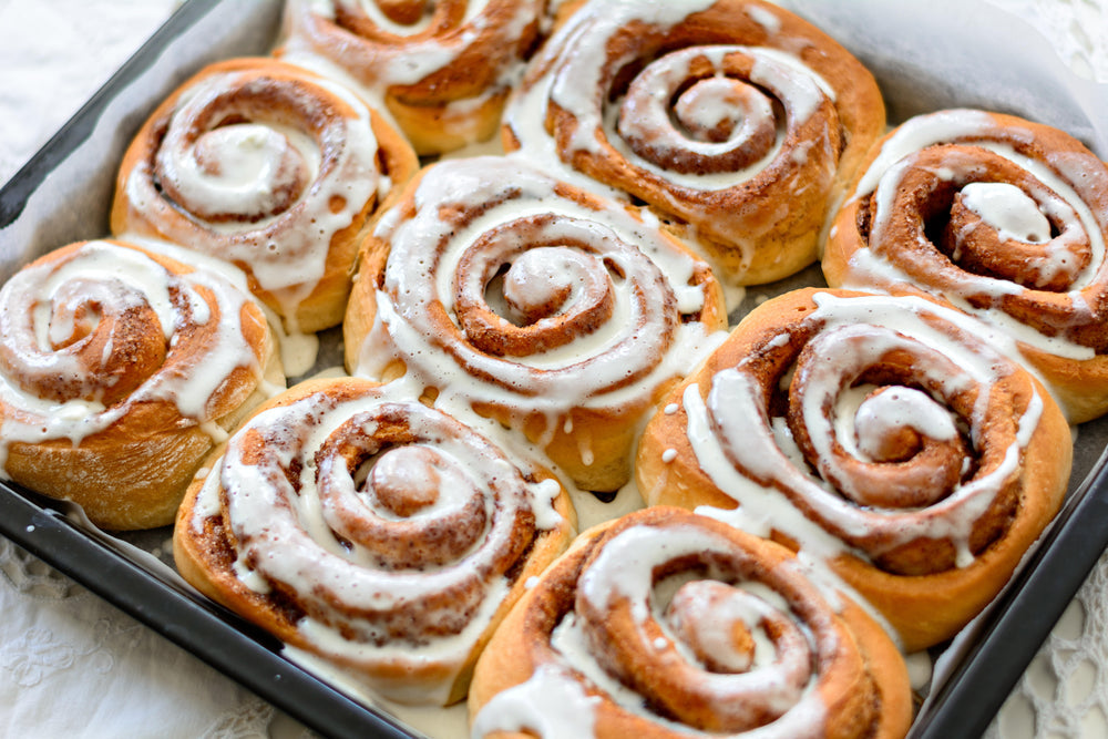 Fresh cinnamon rolls with icing in baking tray.