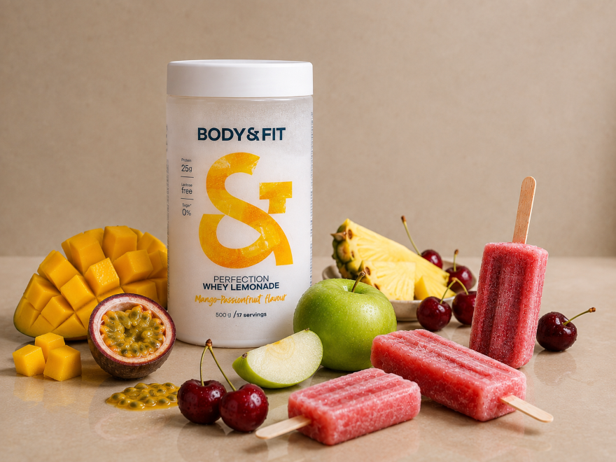 Pot de Body&Fit Perfection Whey Lemonade saveur Mangue-Fruit de la Passion, entouré de glaces aux fruits roses, de cerises, de pomme et d'ananas.