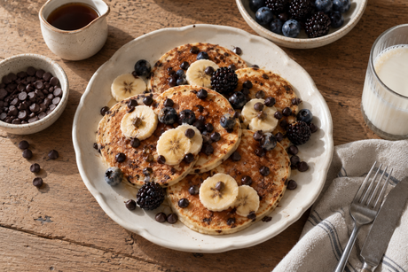 Protein Pancakes mit Bananenscheiben, Heidelbeeren und Choco Drops auf einem Teller