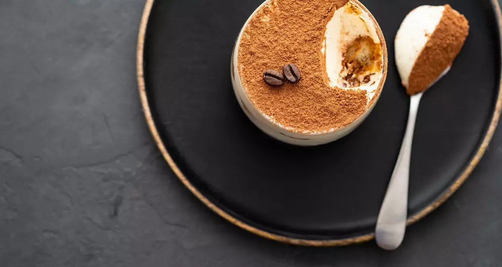 Tiramisu dessert met cacao en koffiesmaak op zwart bord.