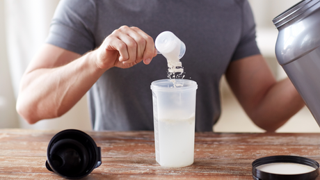 Mann bereitet Proteinshake mit Pulver und Wasser zu.