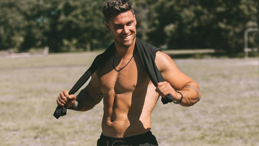 Homme torse nu souriant dans un parc ensoleillé.
