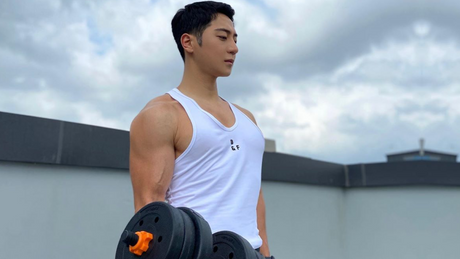 Man in tanktop traint biceps met halters buiten.