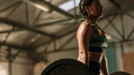 Fit woman lifting barbell in industrial gym, glistening with sweat.