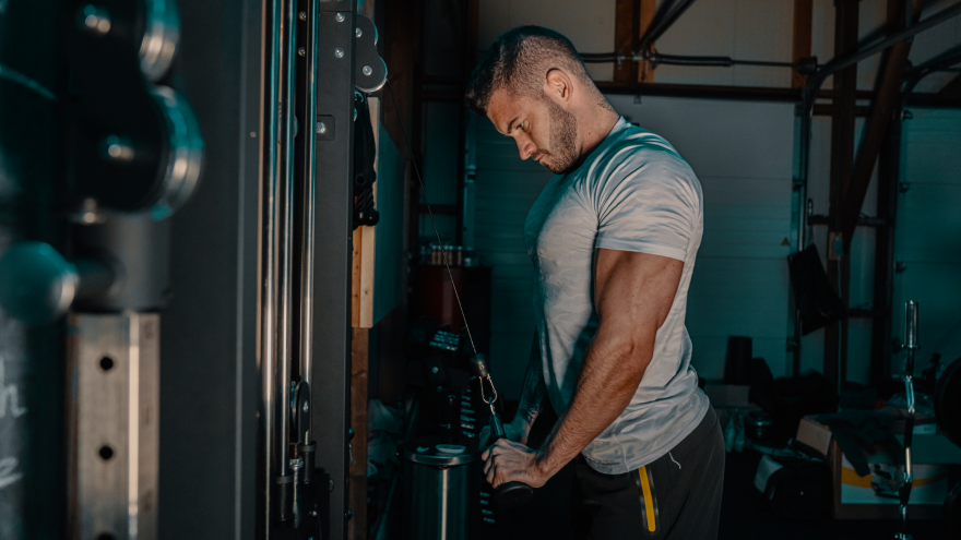 Man traint triceps aan kabelmachine in donkere gym.