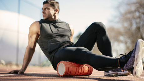 Homme utilisant un rouleau de massage sur un terrain de sport.