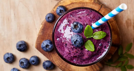 Top view of blueberry smoothie with straw and mint garnish.