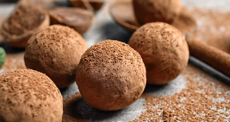 Cocoa protein truffles dusted with powder on grey textured surface.