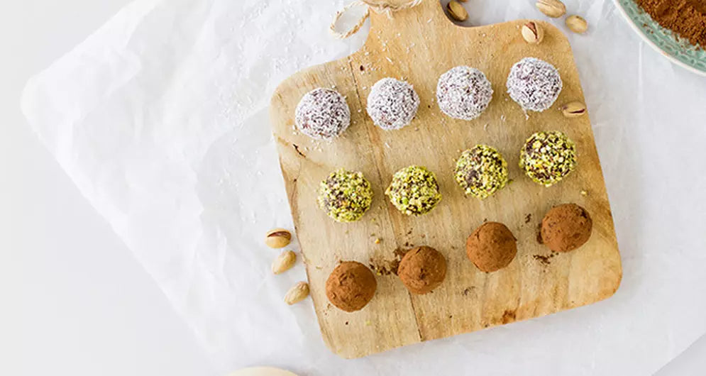Assorted energy balls coated in cocoa, pistachio, and coconut.