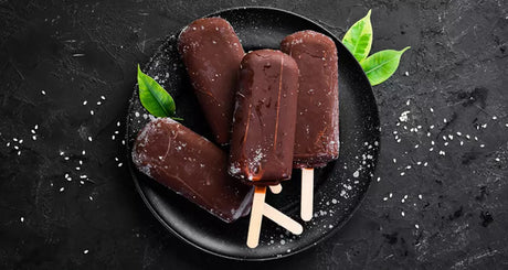 Dunkle Schoko-Eisriegel auf schwarzem Teller mit Minzblättern garniert.