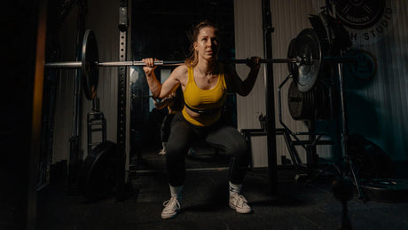 Frau macht Kniebeugen mit Langhantel im Fitnessstudio.