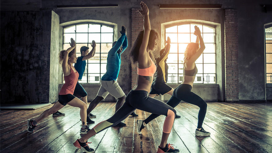 Fitnessgruppe macht Ausfallschritte in hellem Loft-Studio.
