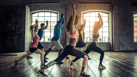 Group fitness class performing lunges in gym studio.