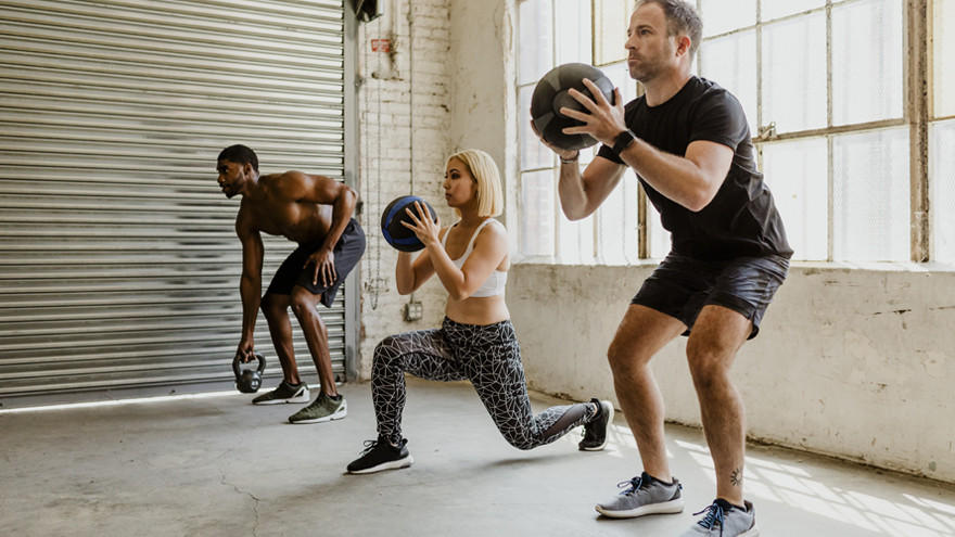 Drie mensen trainen met gewichten in industriële gym.