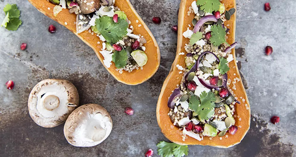Gefüllte Butternut-Kürbishälften mit Quinoa, Gemüse und Granatapfelkernen auf Blech.
