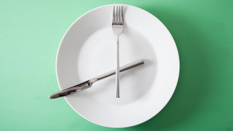 Fork and knife forming clock on white plate.