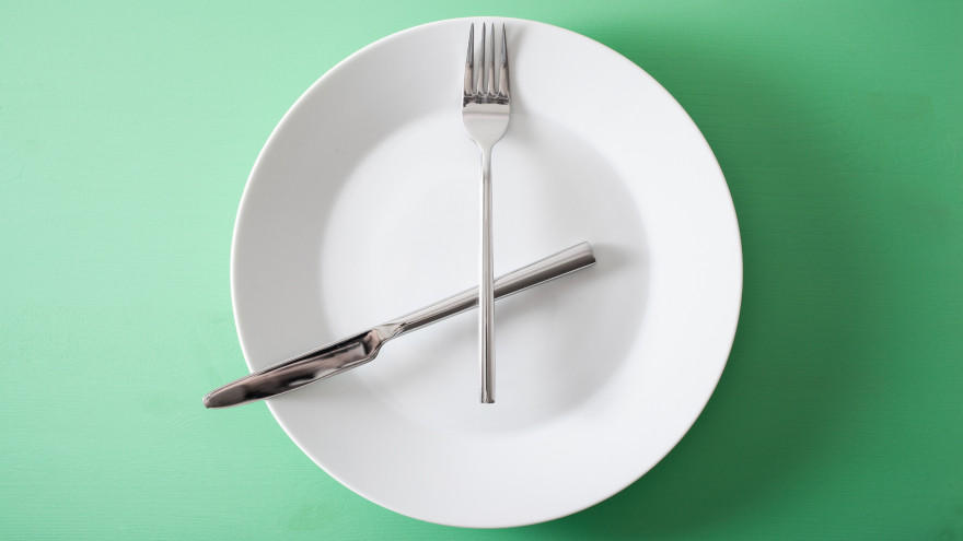 Fork and knife forming clock on white plate.