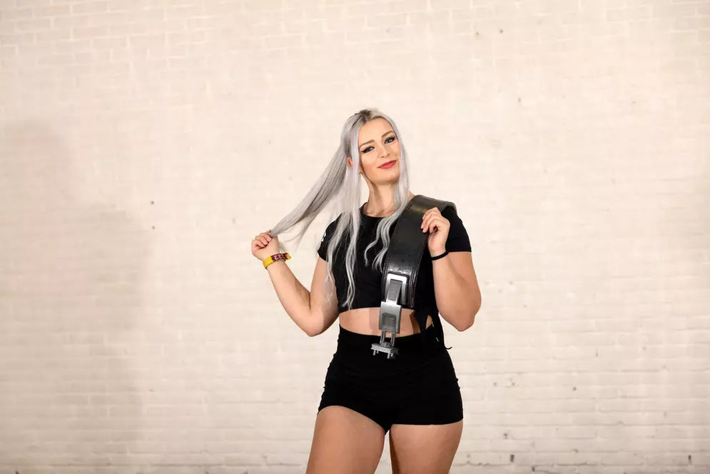 Woman in fitness gear holding lifting belt and smiling.