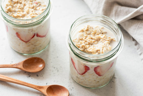 Overnight Oats mit Erdbeeren in Einmachgläsern und Holzlöffeln.